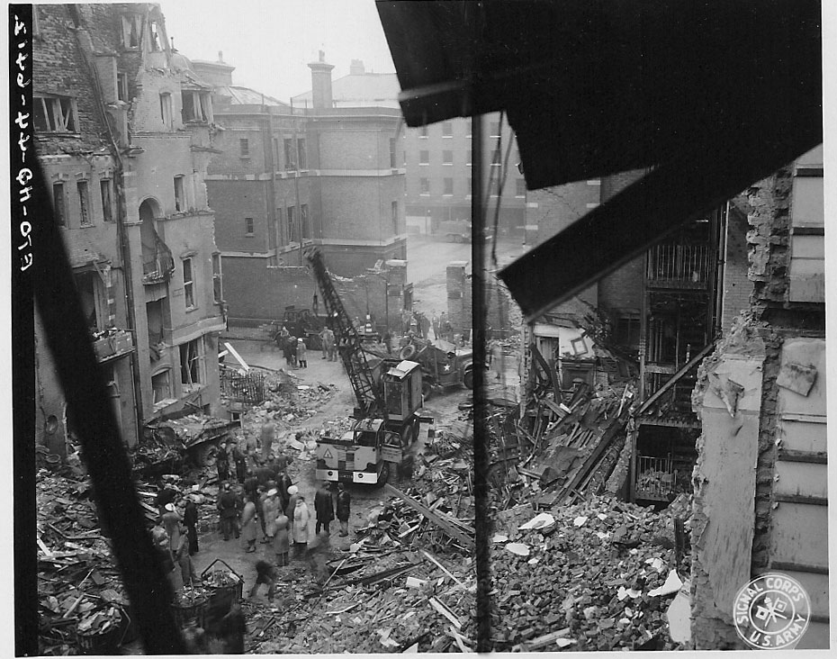 Response crews begin to clean up the damage.  In the background is Turks Row, to the left is the south side of Sloane Court East and to the right is the north side.  After the war, these buildings were replaced. ID #: ETO-HQ-44-6412
